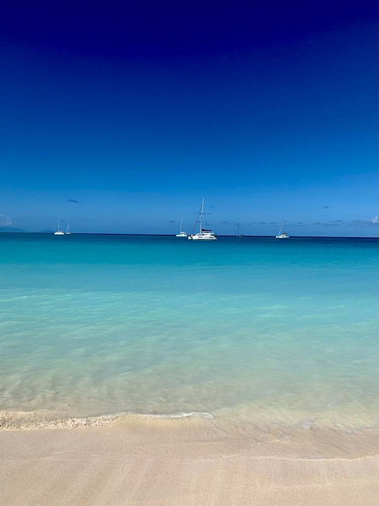 Tranquil pristine beach with sailboats on the horizon in Antigua and Barbuda.